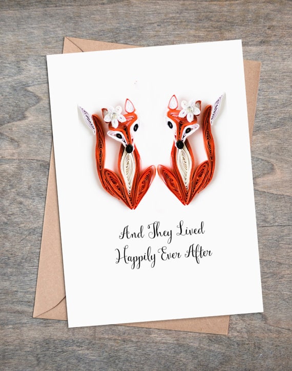 White card with two orange and white foxes with a white flower on their heads made of paper, with black font below them that says "and they lived happily ever after". 