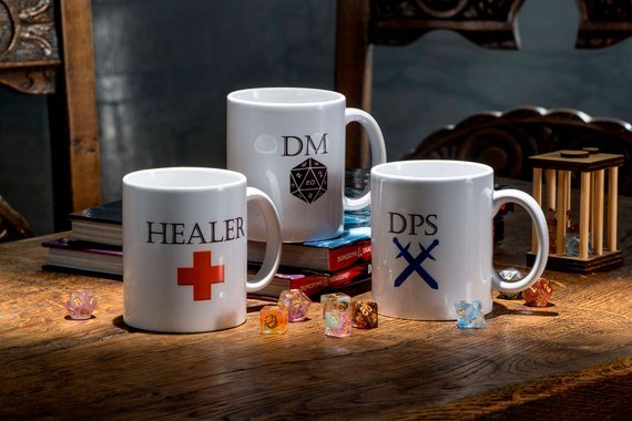 Three coffee mugs shown, one with a red cross that says HEALER, one that says DM and another that says DPS, with two swords crossed. 