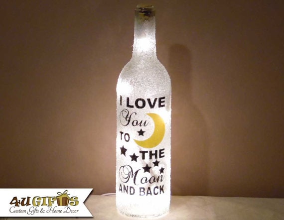 Clear lit up wine bottle with lights in it with black font that says I love you to the moon and back with black stars around the font and a yellow cresent moon. 