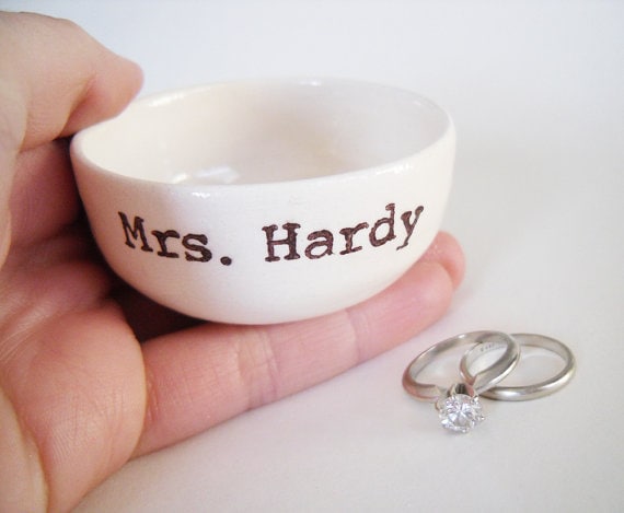 Small white ring dish with black fonr that says Mrs. Hardy.. with two rings laying beshide it. 