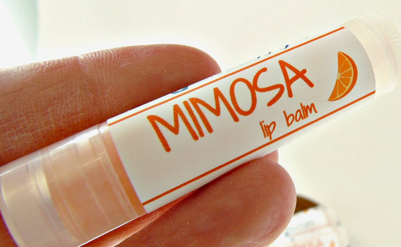 Close up of fingers holding lop balm that says MIMOSA lip balm on it. 