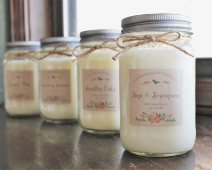 Four mason jars filled with white candles, each with a label of the company with a bird and flowers on it. 