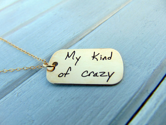 Dog tag style gold necklace with black engraving that says my kind of crazy. 
