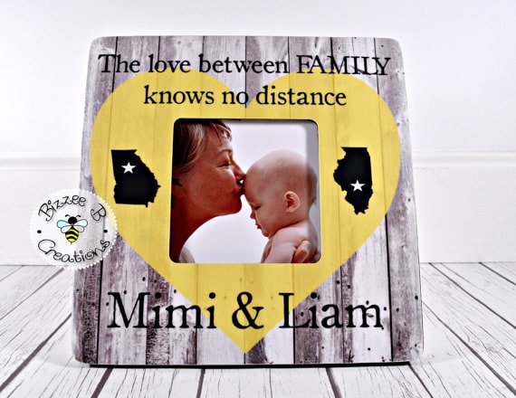 Wooden frame that says The love between family knows no distance with states on the side with a photo of a grandma kissing a baby. 