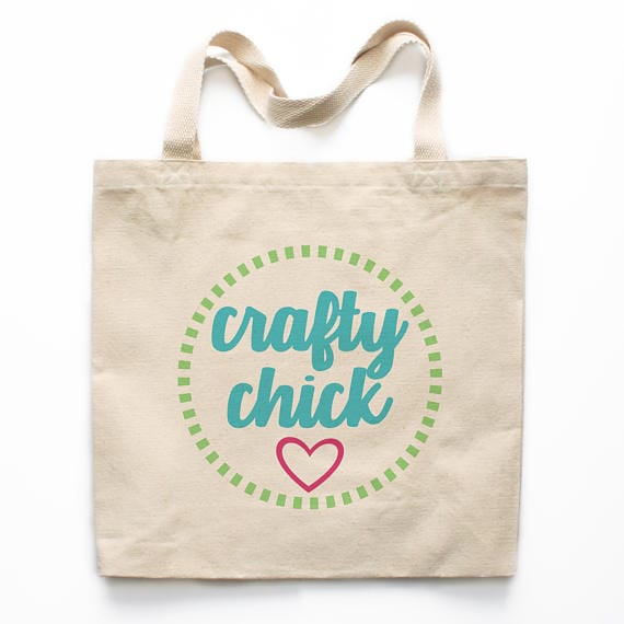 White tote bag with print that says crafty chick in blue font with a green circle around it and a pink heart below it. 