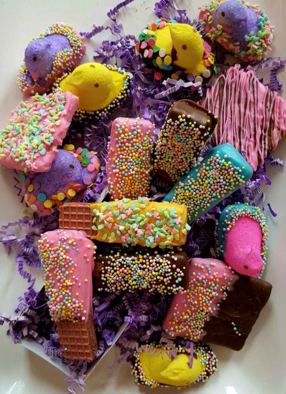 Various colorful chocolates, wafer cookies covered in dark and pink chocolate icing with colorful sprinkles, peeps dipped in chocolate and sprinkles. 