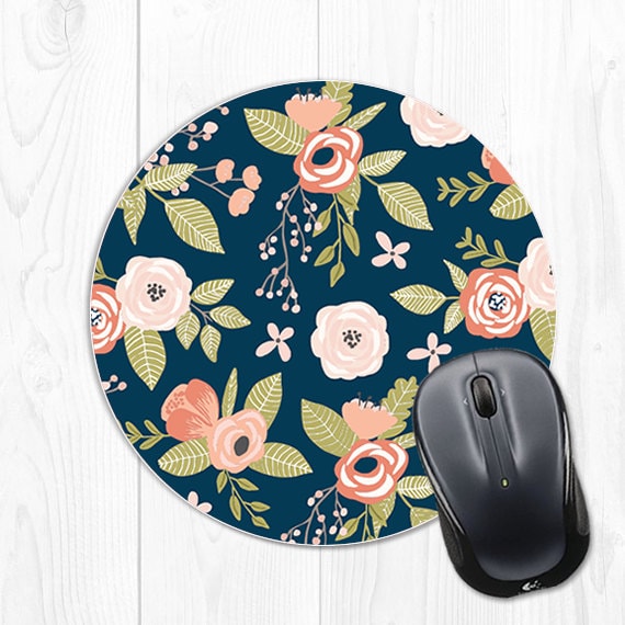Navy round mouse pad with pink roses and green leaves all over it, with a black computer mouse halfway on the mouse pad. 