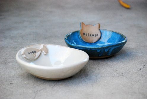 Two cat bowl dishes, one white with a fish on it and one blue with a cats head on it. 