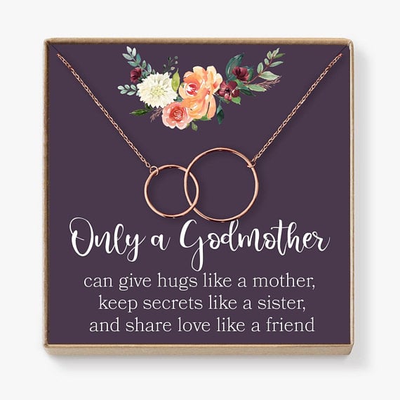 Mother’s Day Gifts for Godmothers: Gold interlocking circle necklace that says only a godmother can give hugs like a mother, keep secrest like a sister, and shar love like a friend on the black paper the necklace is attached to. 