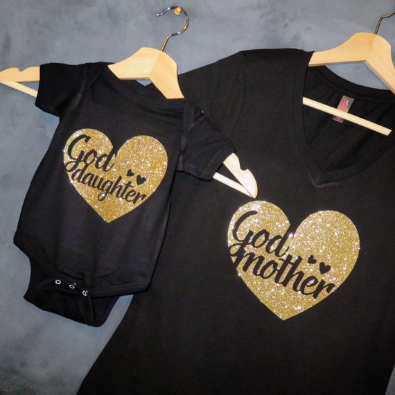 Black matching shirts, one onesies and one t-shirt for an adult. Both with gold sparkly hearts on it, onesies says god daughter and large shirt says god mother. 