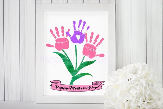 White framed artwork showing pink handprint, purple handprint, and another pink hanrdprint made to look like flowers with black font below that says Happy Mother's Day! 