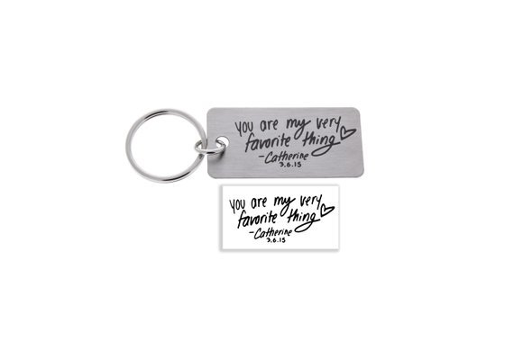 Silver keychain engraved with black font of someone's handwriting. 