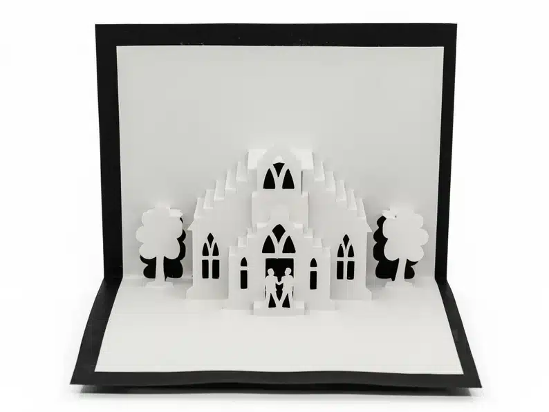 Black and white pop out card of a church and two men on it. 