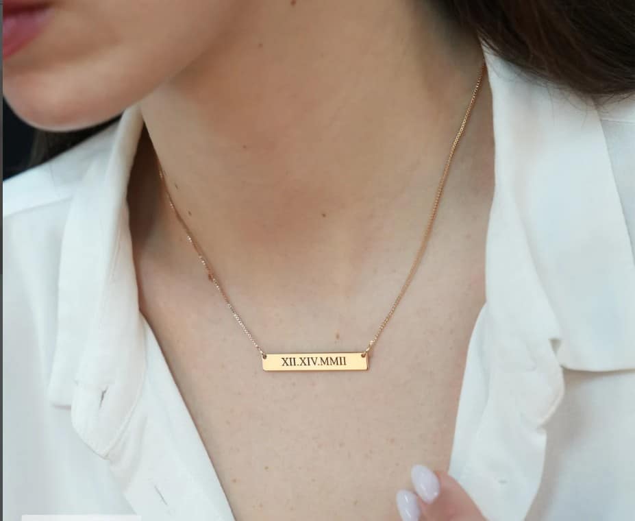 Women wearing a gold rectangle necklace with roman numerals on it. 