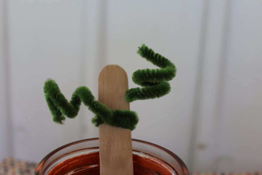 Close up of popsicle stick with green pipe cleaner on it. 