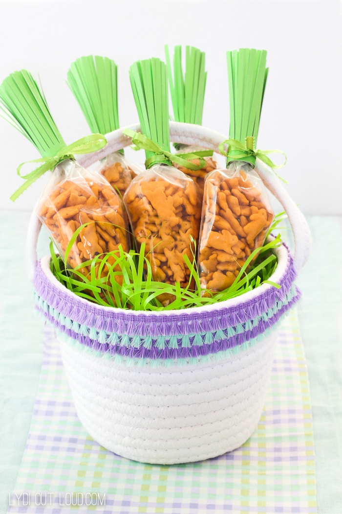 showing a basket full of Fringe Easter Basket & Carrot Easter Treat Bags filled with bunny shaped crackers. 