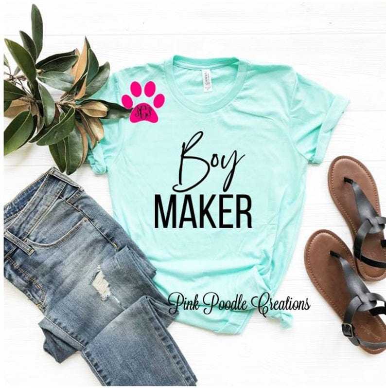 Light blue with black font that says Boy maker. with jeans and brown sandles beside the shirt.