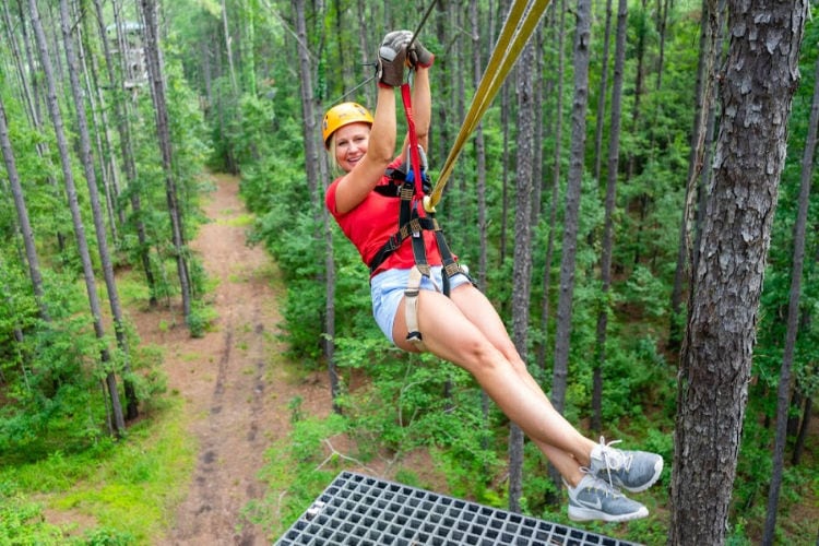 Charleston Zipline | Blonde woman with red shirt, blue shorts and grey sneakers on a zipline amongst green trees