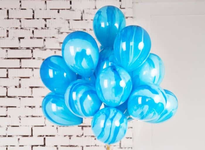 bundle of blue balloons in front of a white brick wall, with gold ribbon