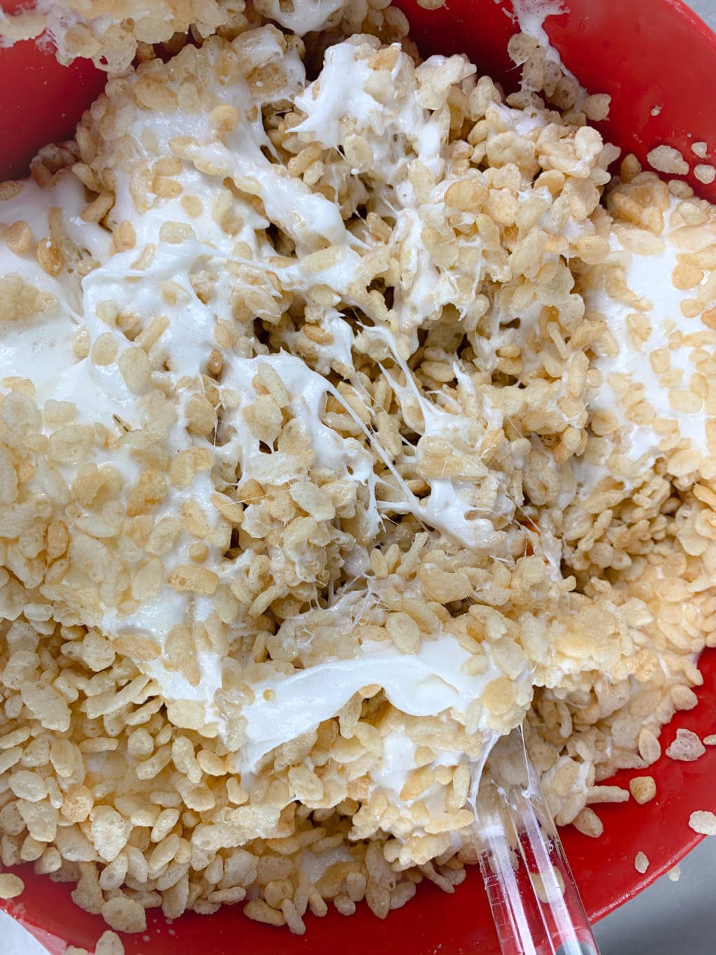 Showing rice krispies mixed with melted marshmallows in red bowl. 