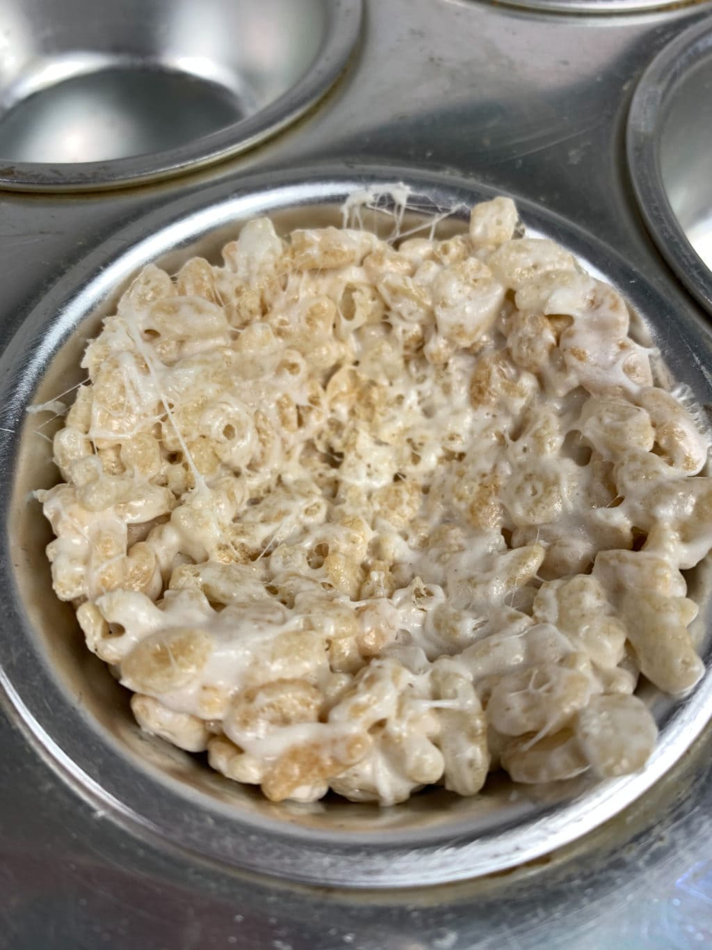 Marshmallow and rice krispes mixed together being placed in muffin tins.