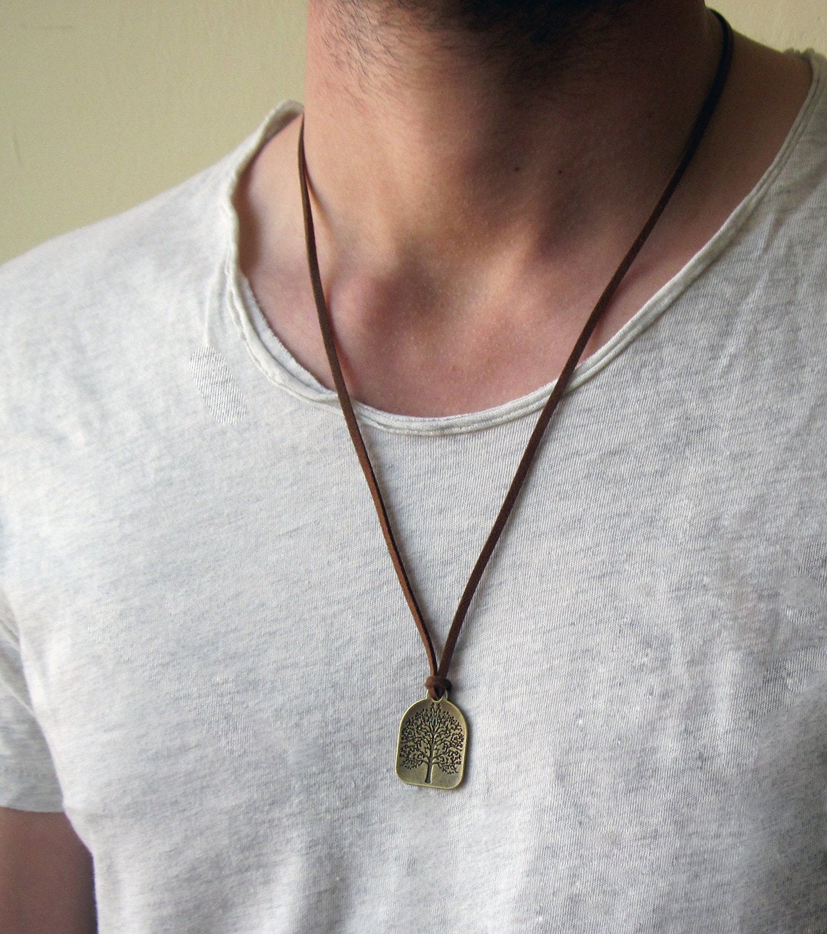 Close up of a mans chest with a brown leather necklace with a silver tree of life charm on the end. 