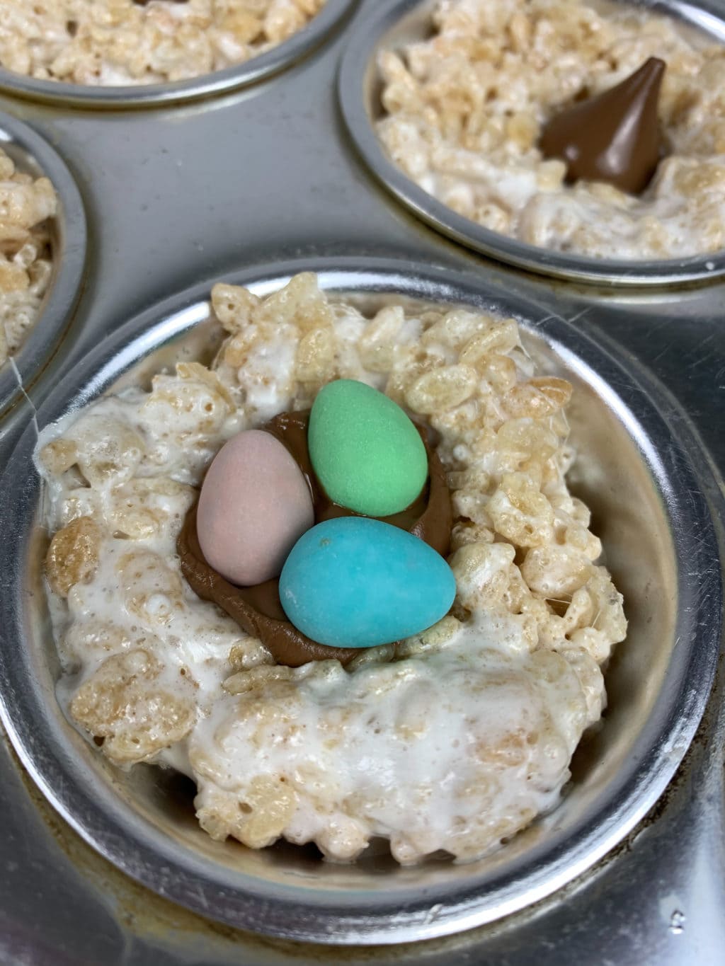Close up of one rice krispie nest with melted chocolate in middle and three mini eggs: pink, blue, and green in the middle. 