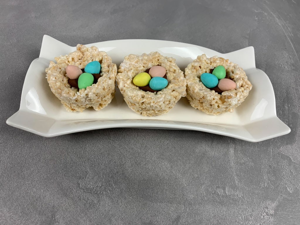 Three Rice Krispie Easter Egg Nests showing the rice krispies shaped into nests, with three colorful mini eggs on top of melted chocolate in the middle. 