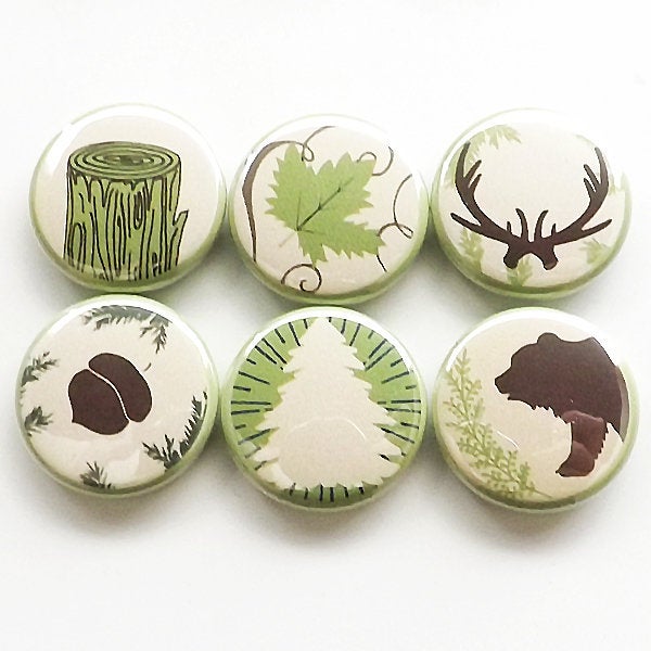 Six round white hunting themed magnets, each with various hunting stuff on it like deer antlers, bear, tree, stump, acorn, and a leaf. All brown and green. 