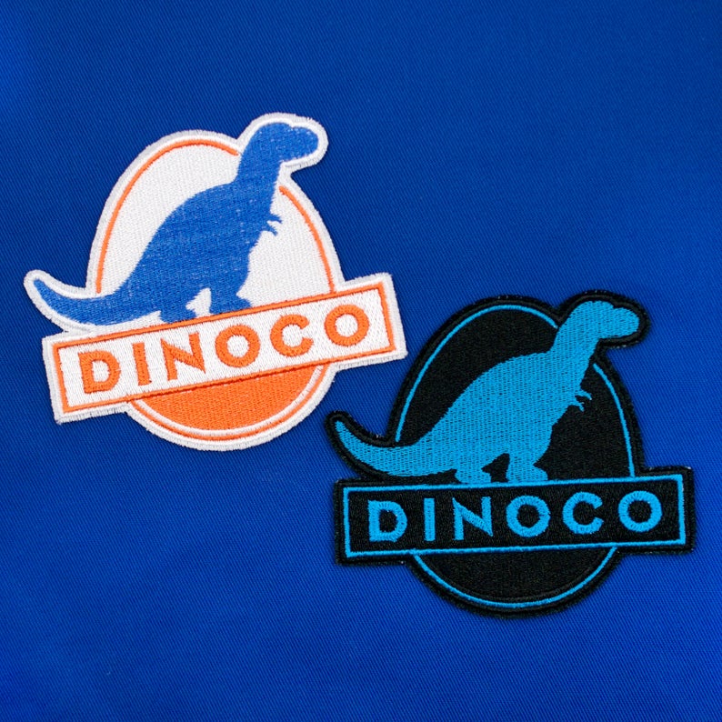 Blue background with two Dinoco patches shown, one white and orange with a  light blue dinosaur on it and one black and blue.