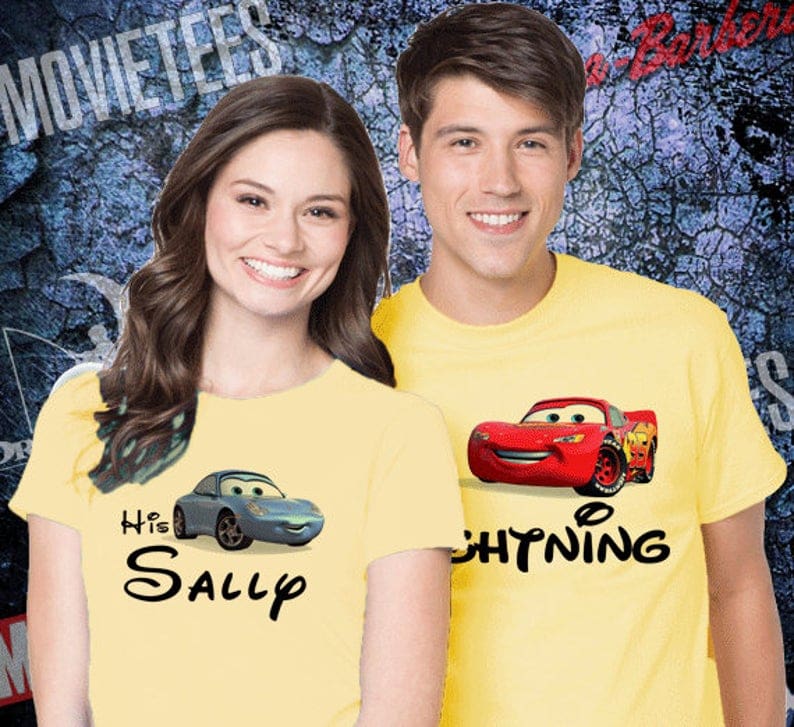 Woman and man smiling both wearing yellow t-shirts, the woman wearing one that says HIS SALLY with a blue car on it and the other with lightning McQUeen on it.