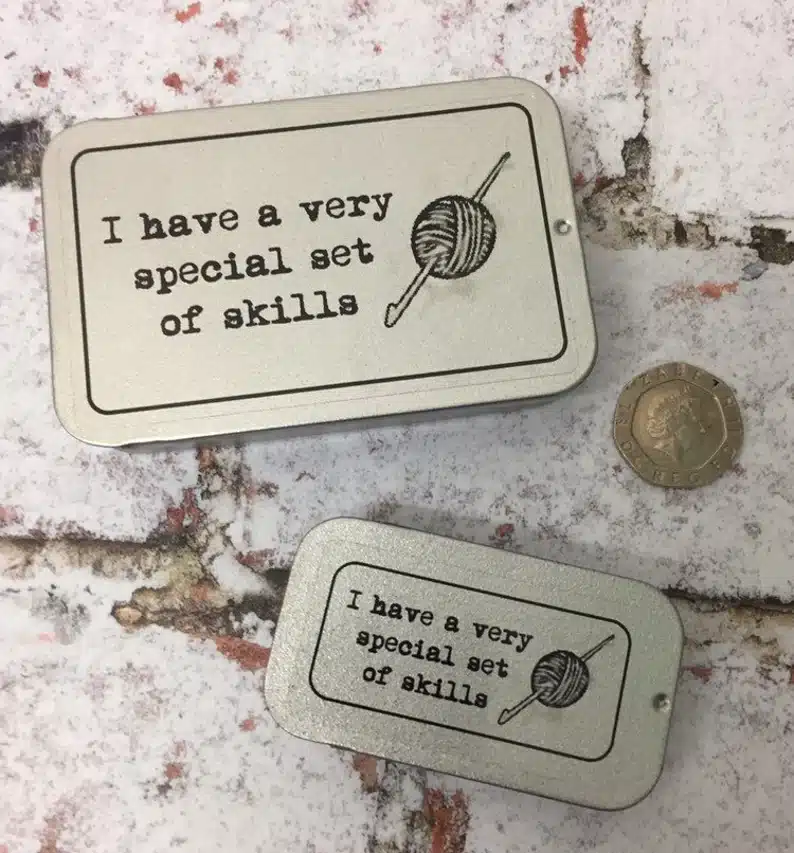 Two silver tins that say "I have a very special set of skills" with a drawing of a yarn and needle on it.