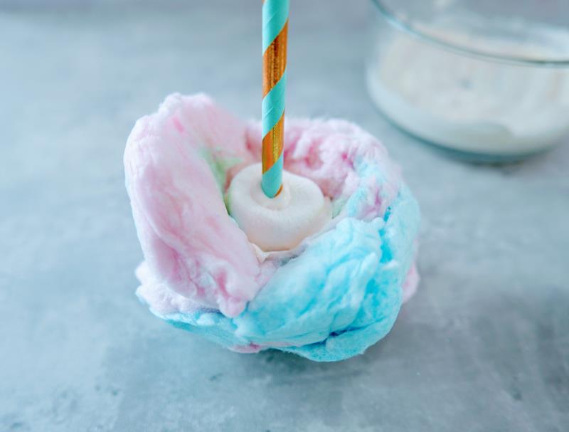 Marshmallow on straw being pushed into cotton candy. 