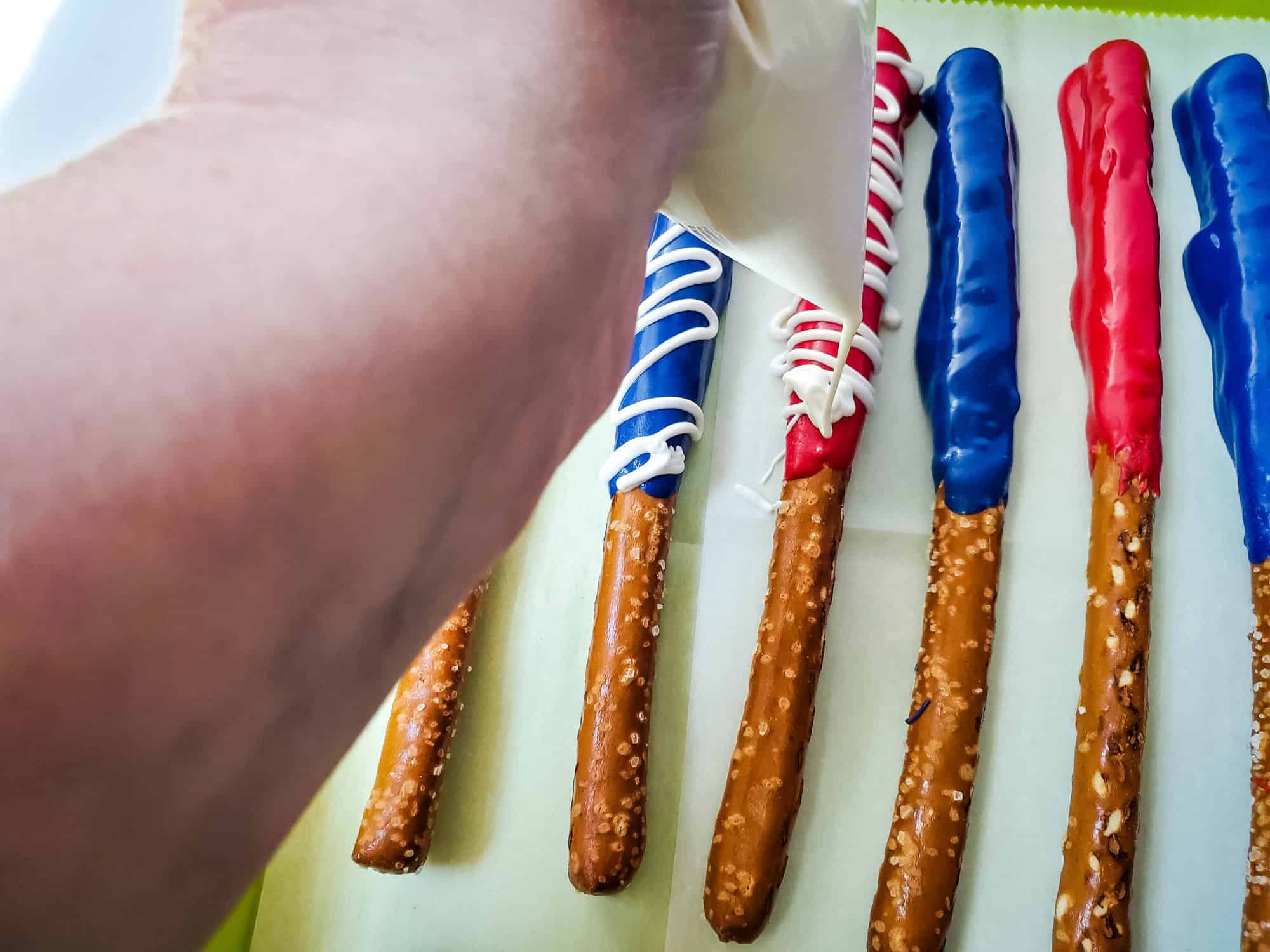 melted white chocolate in a Ziplock piping bag drizzling over coated pretzel rods