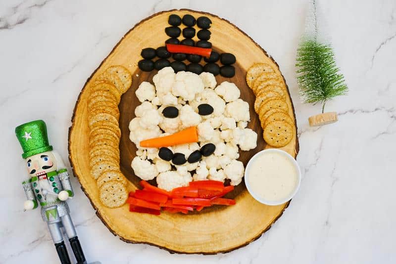 snowman veggie tray pictured on a live edge charcuterie board