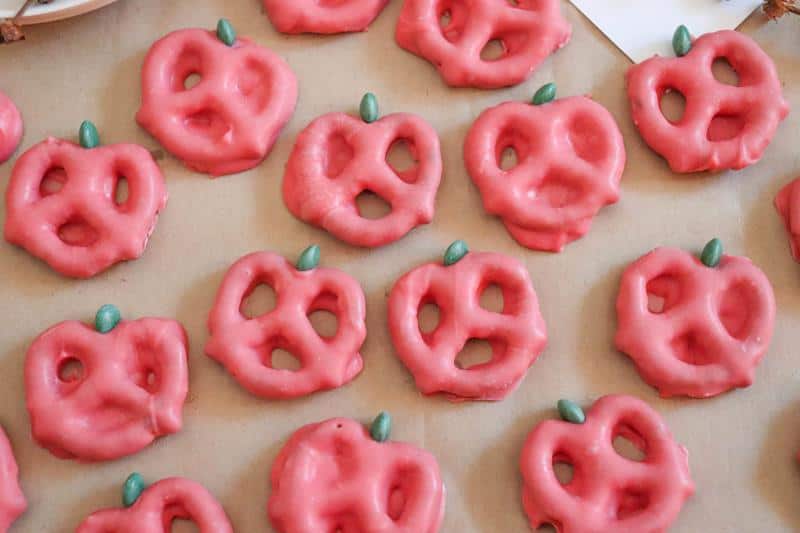 close up of completed apple pretzels covered in red candy melts and green M&M on top. 