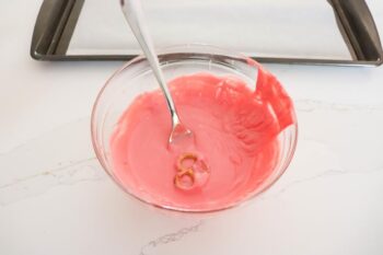 above view of glass bowl with melted red candy melts with fork placing pretzel in candy.