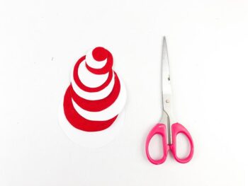 above view showing red and white construction paper cut out in circles with pink handled scissors beside. 