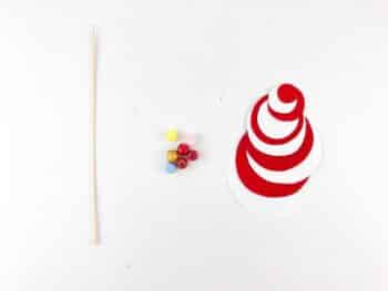 Above view of BBQ stick, colorful beads, and circled red and white construction paper. 