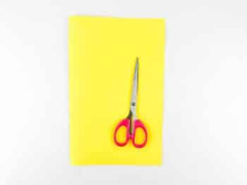 Above view of yellow paper and pink handled scissors. 