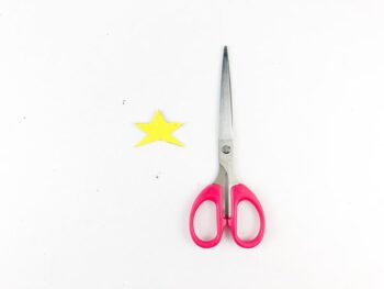 Yellow star cut out from yellow paper with pink handled scissors beside them. 