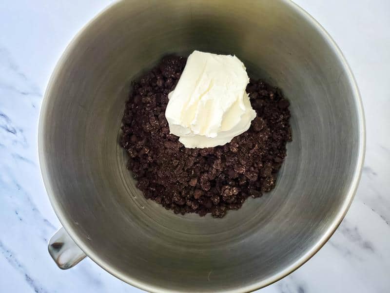 Bowl of crushed Oreos with cream cheese on top about to be mixed together.