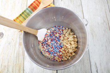 Above view of a mixing bowl with blue, white, and red sprinkles and crushed up golden Oreos. 