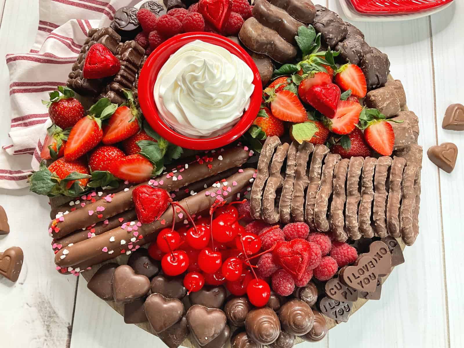 close up photo showing completed snack board with fruit, chocolate hearts, whip cream, chocolate covered pretzels, and chocolate hearts.