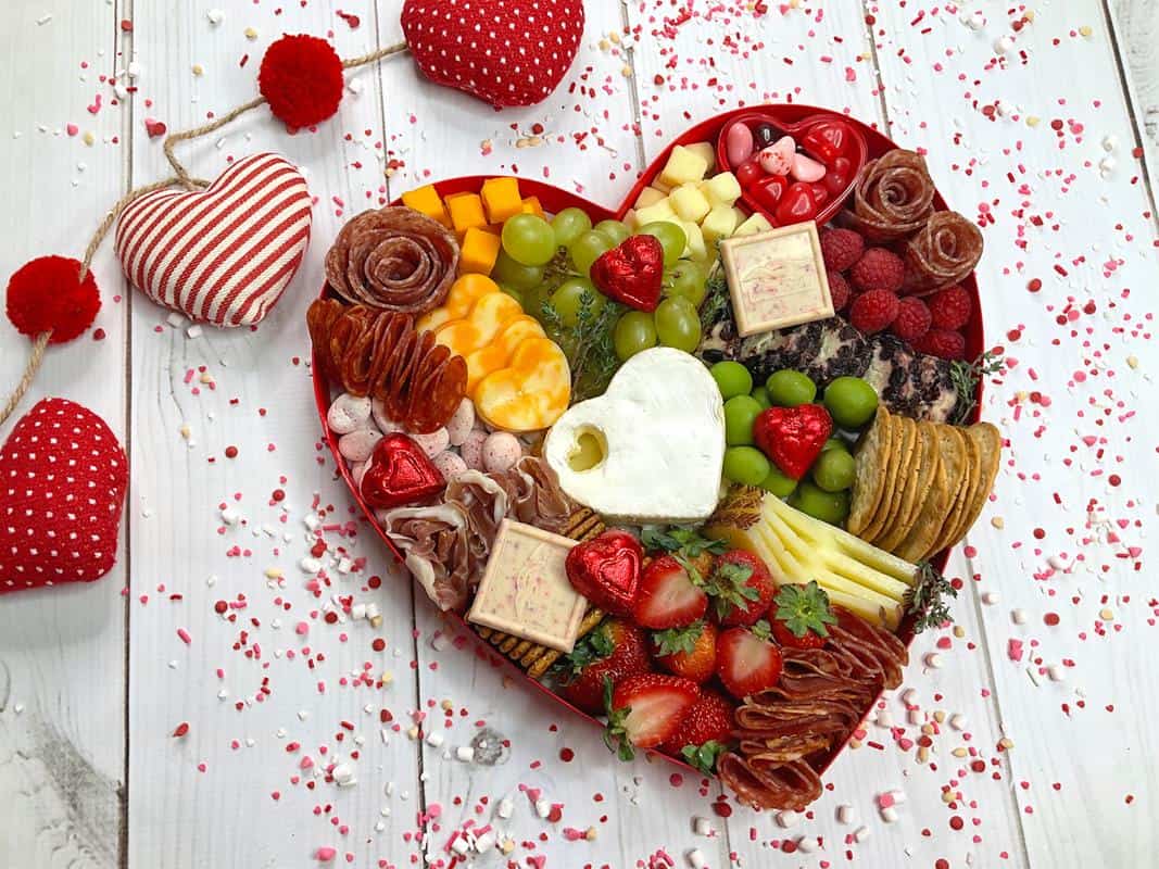 Above view of heart shaped Charcuterie board showing crackers, cheese, meats, fruit, olives and various other savory foods.