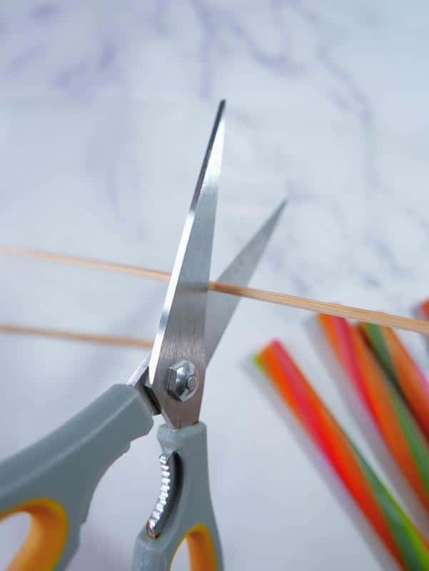 Close up photo of bamboo skewer being cut with scissors. 