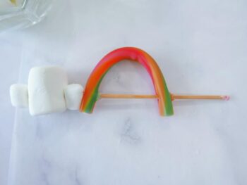 Showing mini marshmallow, regular size marshmallow, mini marshmallow and sweetart candy arched like a rainbow on bamboo skewer. 