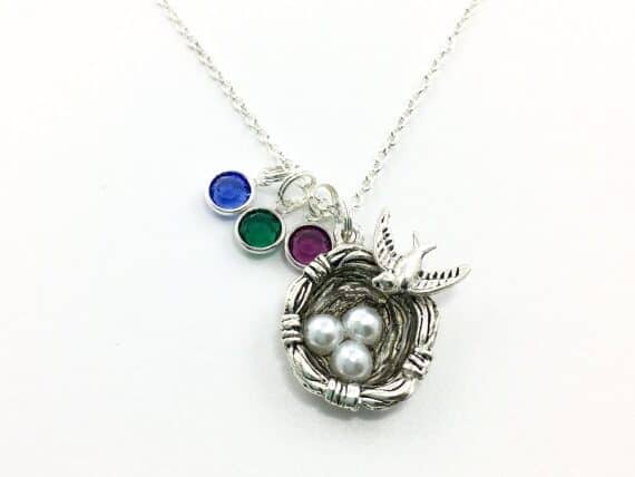 Silver chain with next with three white pearls and a silver bird on the side with three birthstone charms beside it. 