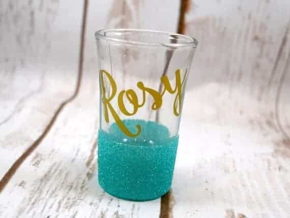 Personalized shot glass, bottom half light blue sparkled and top with gold font that says Rosy. 