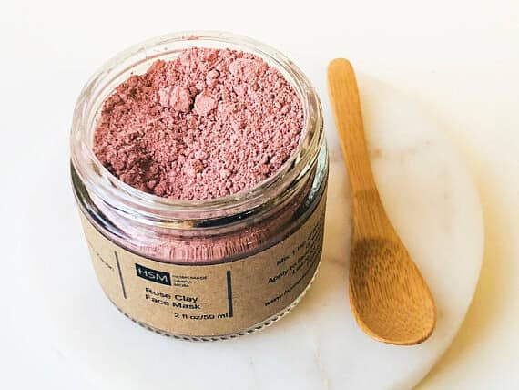 Jar of rose dust clay mask and a little wooden spoon beside it.